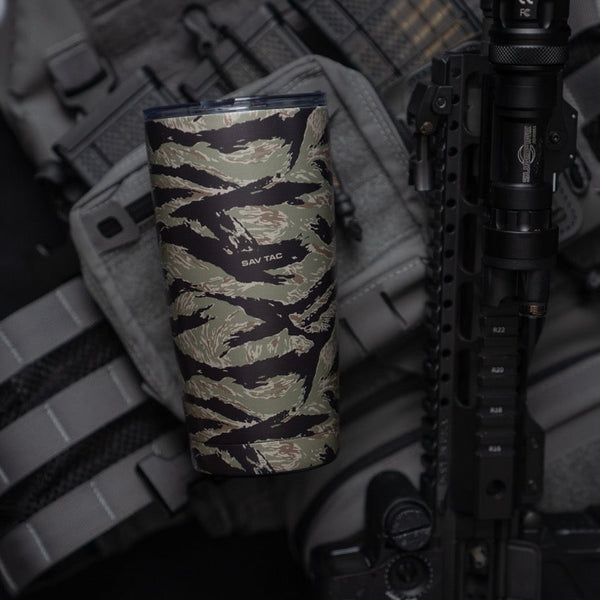 Savage Tacticians camo travel tumbler with SAV TAC logo against tactical gear and rifle