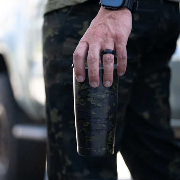 Savage Tacticians camo tumbler held by person in camouflage pants outdoors
