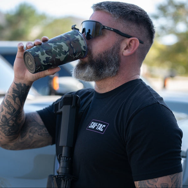 Man in sunglasses wearing Savage Tacticians t-shirt drinks from camouflage tumbler outdoors