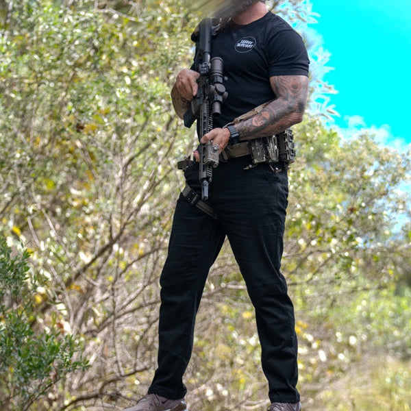 Man in Savage Tacticians t-shirt holding rifle outdoors, tactical gear and forest background