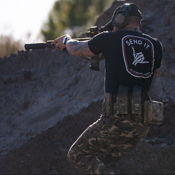 Person in tactical gear with a rifle, wearing the Send it tactical streetwear shirt.