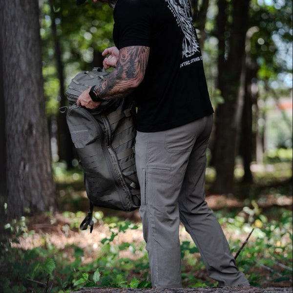 Man wearing Savage Tacticians t-shirt and tactical pants holding backpack outdoors