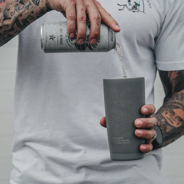 Tattooed man pouring drink into Savage Tacticians branded grey tumbler