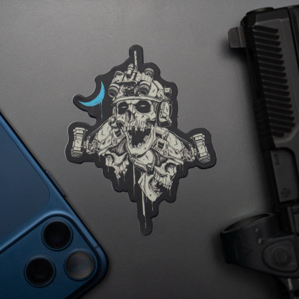 Savage Tacticians skull sticker with night vision helmet on laptop, blue phone and handgun nearby