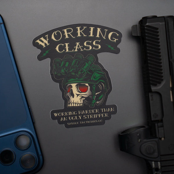 Savage Tacticians skull helmet sticker with 'Working Class' design on a laptop, next to a phone and firearm.