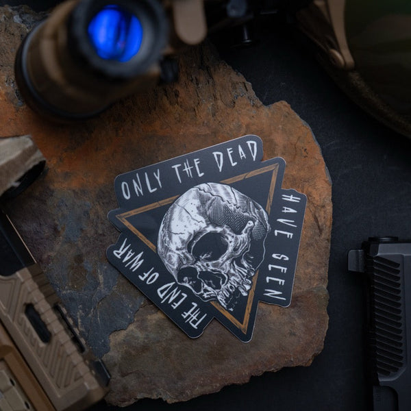 Savage Tacticians sticker with skull design and quote Only the Dead Have Seen the End of War, on rock with tactical gear