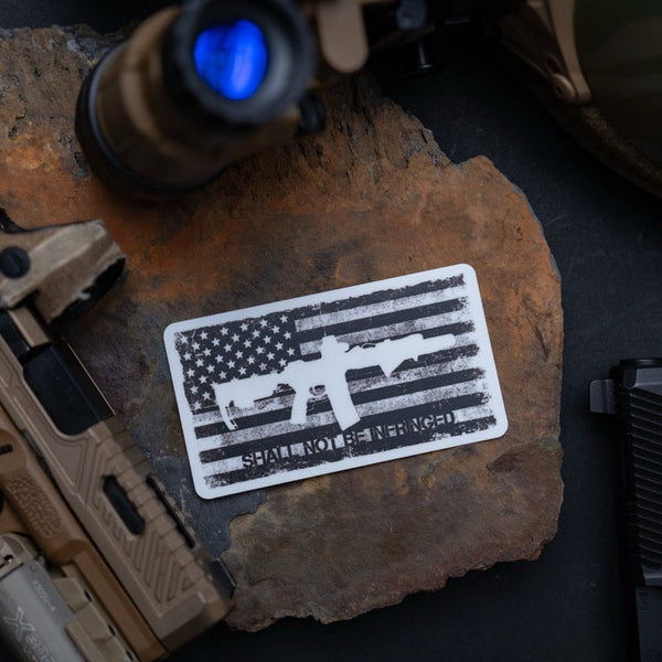 Savage Tacticians sticker with AR-15 rifle and American flag on stone, tactical gear background