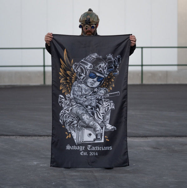 Person with tactical helmet holding Savage Tacticians flag featuring tattooed angel design