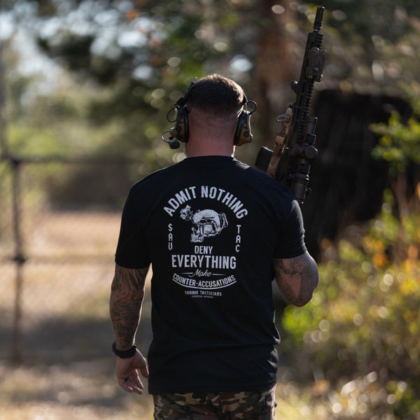 Man outdoors in tactical gear wearing a Savage Tacticians graphic t-shirt, holding a rifle