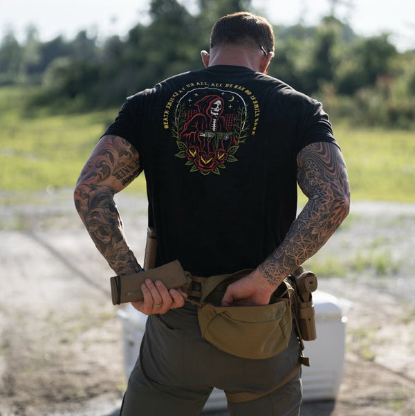 Tattooed man outdoors wearing Savage Tacticians black graphic t-shirt with grim reaper design
