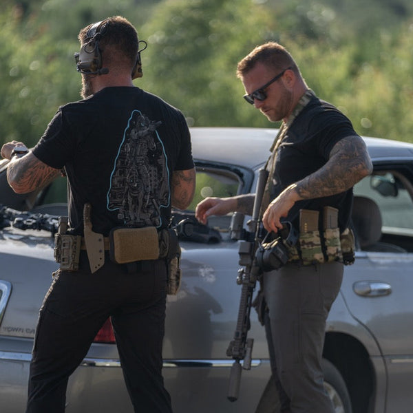 Two men in tactical gear and Savage Tacticians shirts standing by a car outdoors