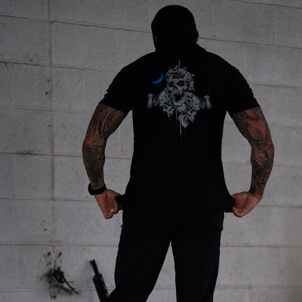 Tattooed man wearing Savage Tacticians black shirt with skull graphic on back
