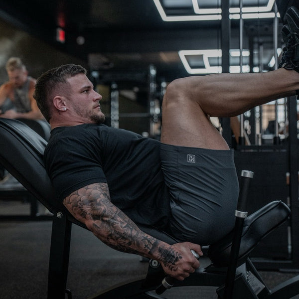 Man lifting weights in gym wearing Savage Tacticians athletic shorts and black shirt
