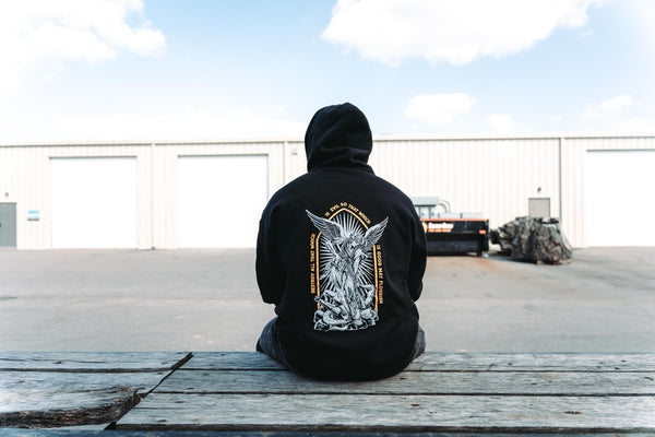 Man seen from behind sitting outdoors in the black Savage Tacticians Saint Hoodie