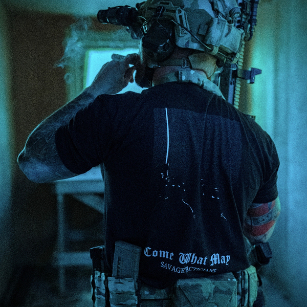 Man in tactical gear wearing a Savage Tacticians shirt with 'Come What May' text visible