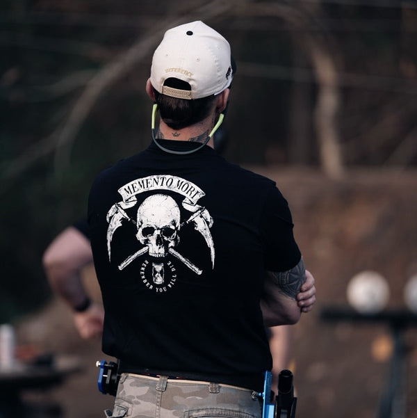 Person wearing a black t-shirt with a skull design and 'Memento Mori' text, standing outdoors.