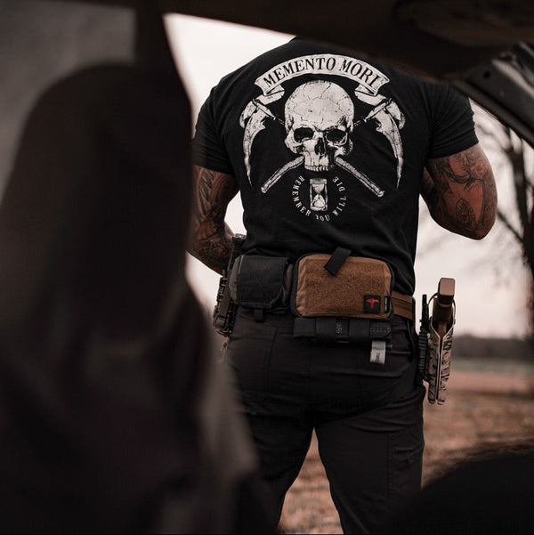 Person wearing a black t-shirt with a skull design and tactical gear outdoors.