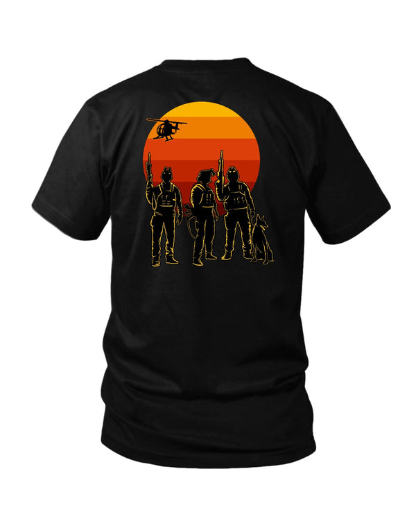 Savage Tacticians Black tee featuring three tactical operator silhouettes and a K9 in front of a layered orange sunset, helicopter overhead.