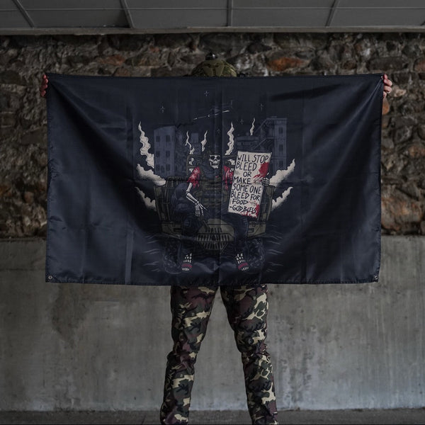 Person in camo pants holding Savage Tacticians flag with skeleton art and urban background