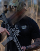 Man in Savage Tacticians t-shirt and camo helmet holding tactical rifle outdoors
