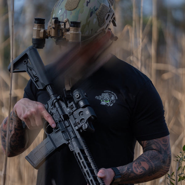 Man in Savage Tacticians t-shirt and camo helmet holding tactical rifle outdoors