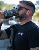 Man in sunglasses wearing Savage Tacticians t-shirt drinks from camouflage tumbler outdoors