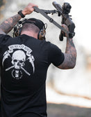 Man holding a rifle with a black t-shirt featuring a skull and scythe design on the back. Memento Mori.