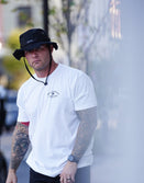 Man wearing Savage Tacticians white t-shirt and black hat, street style, outdoor urban scene