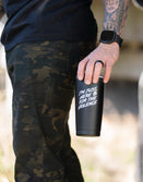 Man with tattooed arm holding Savage Tacticians tumbler, camo pants, outdoor setting