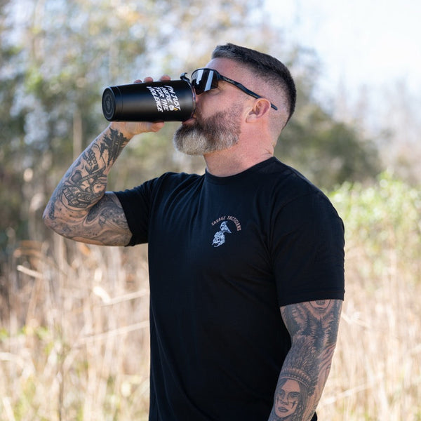 Tattooed man in sunglasses wearing Savage Tacticians shirt drinking from a black tumbler outdoors