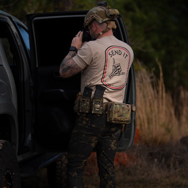 Man in tactical gear wearing Savage Tacticians 'SEND IT' shirt outdoors by vehicle