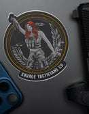 Savage Tacticians sticker featuring armed woman with scales of justice, on laptop near phone and gun