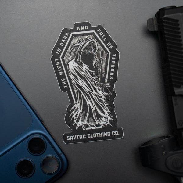 Savage Tacticians sticker with grim reaper design and text, on dark surface near phone