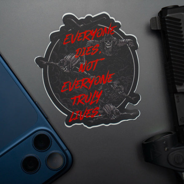 Savage Tacticians sticker with skull design and red text, placed by phone and firearm