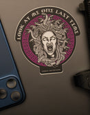 Savage Tacticians Medusa sticker on laptop, beside blue smartphone and gun