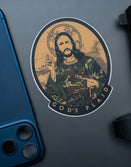 Savage Tacticians sticker of a saint in camo with 'God's Plaid' text, next to phone and pistol