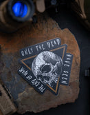 Savage Tacticians sticker with skull design and quote Only the Dead Have Seen the End of War, on rock with tactical gear