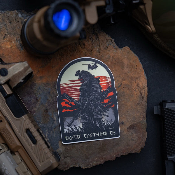 Savage Tacticians sticker featuring a samurai with helicopter, sunset, mountains, and gear