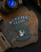 Savage Tacticians Working Class sticker with skull helmet on stone, tactical gear nearby
