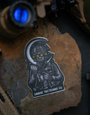 Savage Tacticians night vision operator sticker on rock with tactical gear background