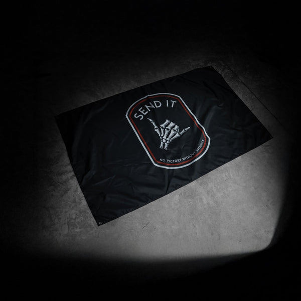 Savage Tacticians 'Send It' black flag with skeleton hand design on a concrete floor