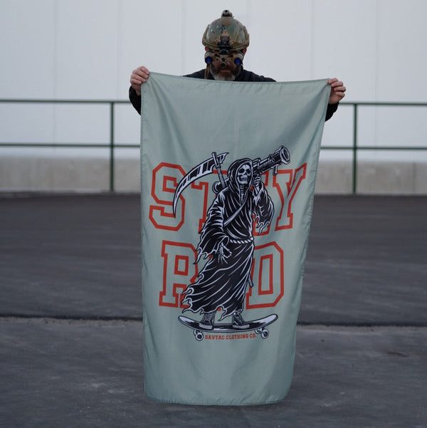Person with tactical helmet holds Savage Tacticians Stay Rad flag featuring Grim Reaper graphic.