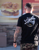 Savage Tacticians black graphic t-shirt with airplane design worn by tattooed man in camo shorts