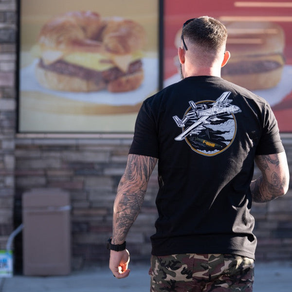 Savage Tacticians black graphic t-shirt with airplane design worn by tattooed man in camo shorts
