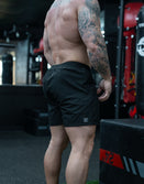 Muscular man with tattoos wearing Savage Tacticians black athletic shorts in gym