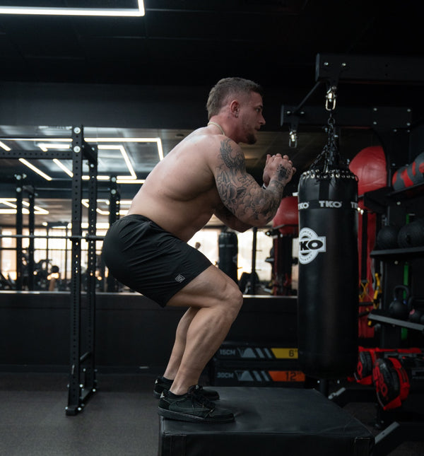 Man wearing Savage Tacticians shorts doing box jumps in a gym with punching bags