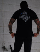Tattooed man wearing Savage Tacticians black shirt with skull graphic on back