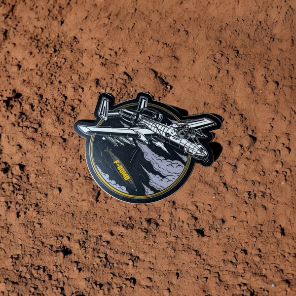 Savage Tacticians A-10 jet sticker with F-BOMB text on a textured brown surface