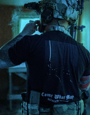 Man in tactical gear wearing a Savage Tacticians shirt with 'Come What May' text visible