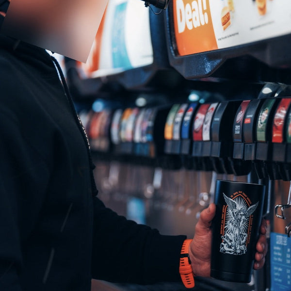Person filling a Savage Tacticians tumbler at a soda fountain, wearing black hoodie and orange watch